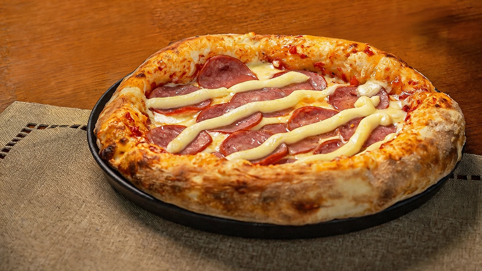 Pizza calabresa com catupiry recém-saída do forno, fatias de calabresa douradas e risco de catupiry por cima, borda dourada