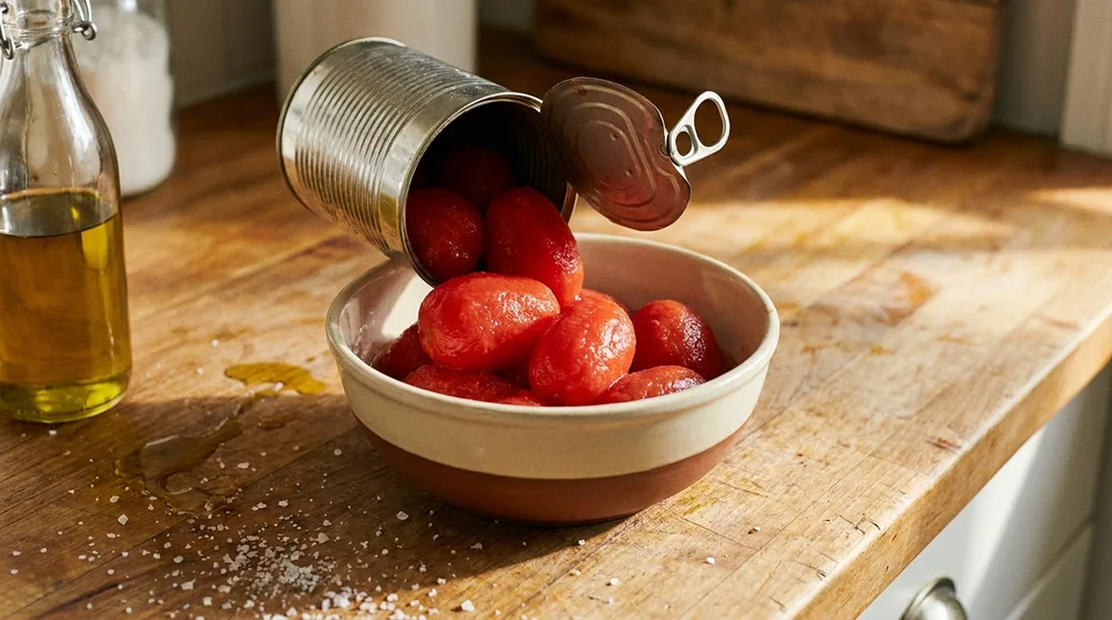 Tomates pelados escorrendo de uma lata aberta para dentro de uma tigela de cerâmica
